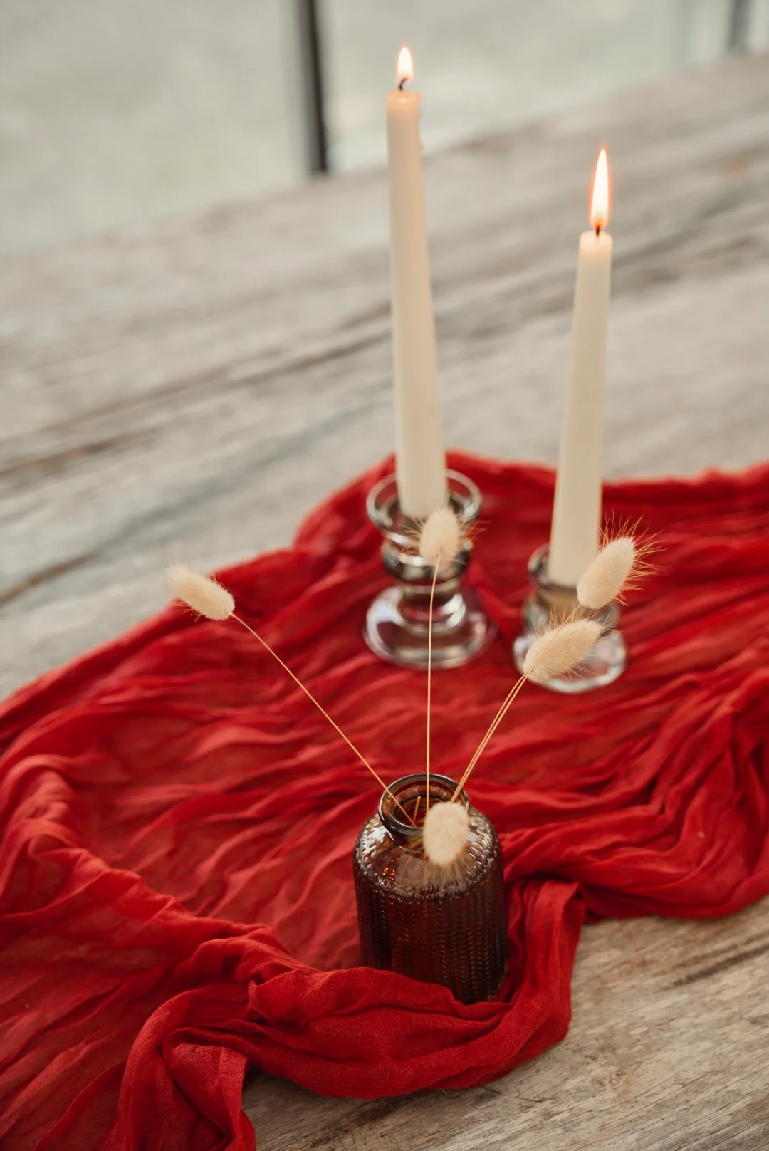 Roter Tischläufer mit brennenden Kerzen und Trockenblumen auf einem Holztisch